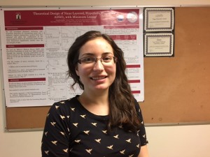 Woman with dark hair, glasses and black printed blouse stands in front of a research poster