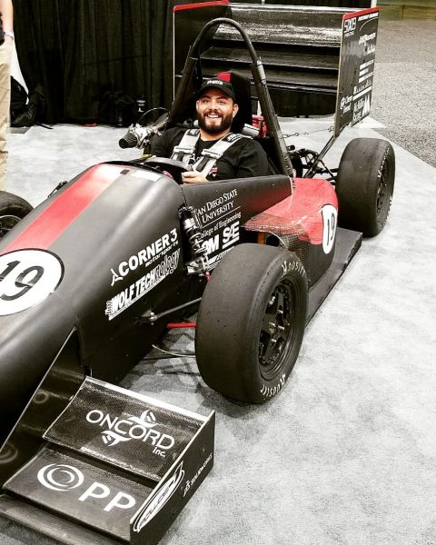 Man wearing a baseball cap sits in a black and red race car