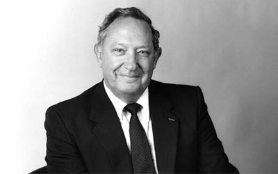 A man in a black suit and tie smiles at the camera