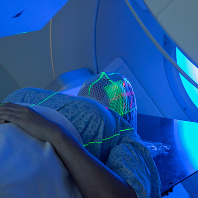 Patient inside a medical apparatus with bright green laser alignment patterns on their face.