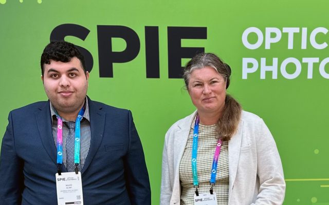 Waleed Al Any and Lyuba Kuznetsova stand in front of Green banner with the letters SPIE Optics Photo.