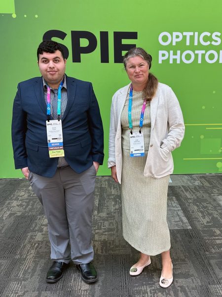 Waleed Al Any and Lyuba Kuznetsova stand in front of Green banner with the letters SPIE Optics Photo.